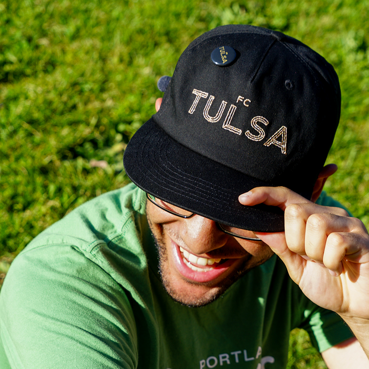 a guy wearing a black fc tulsa hat